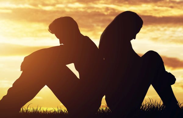 Silhouette of distressed-looking couple in need of counselling therapy sit back to back with yellow sunset behind them.