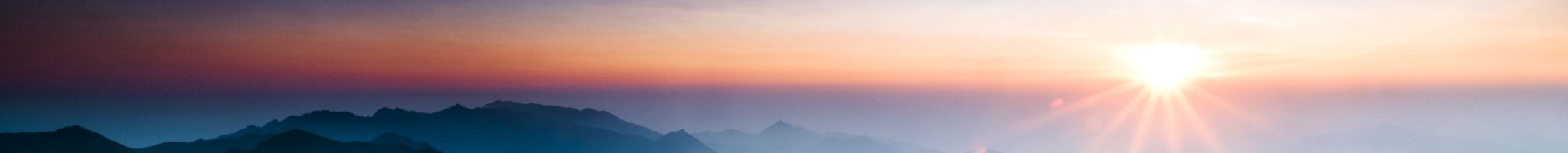 The sun peaks above the clouds and shines down on the shadowy mountains.